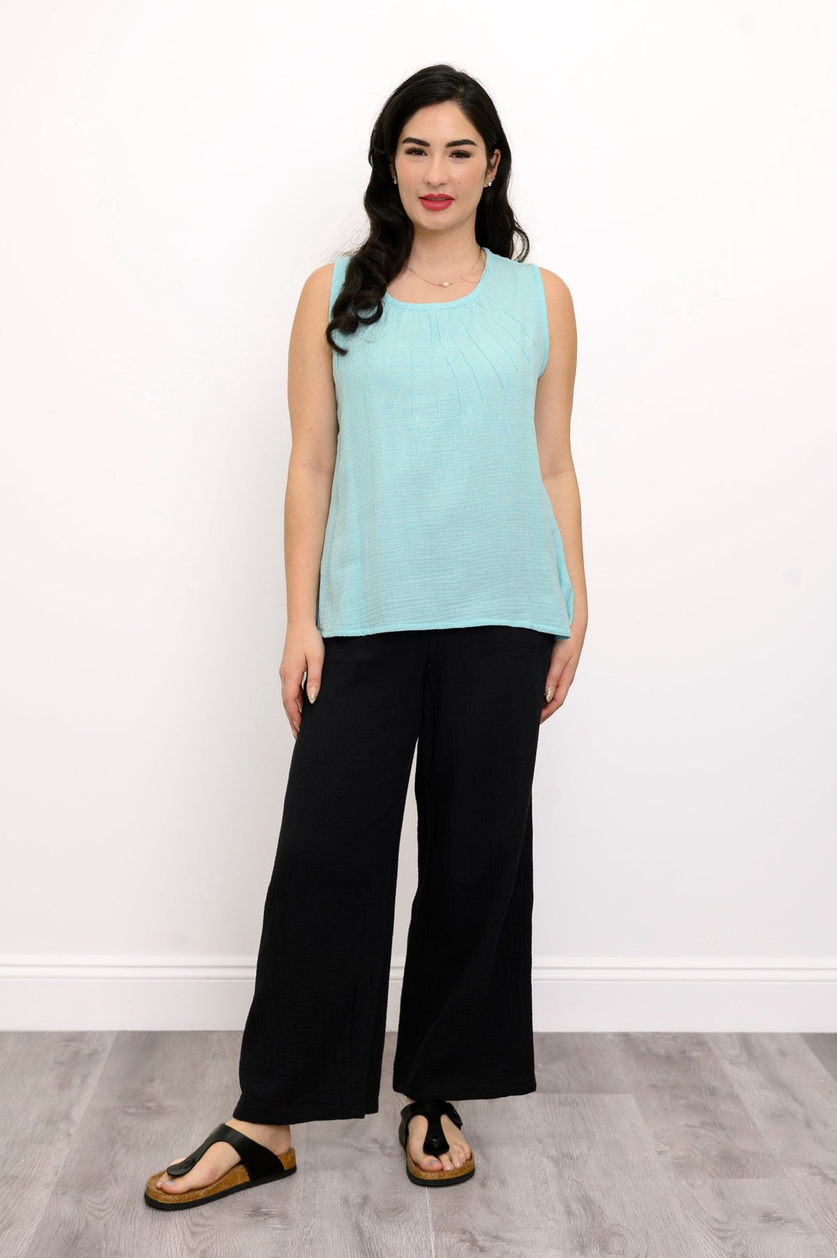 Woman wearing a light blue sleeveless top and black pants against a white background, front view