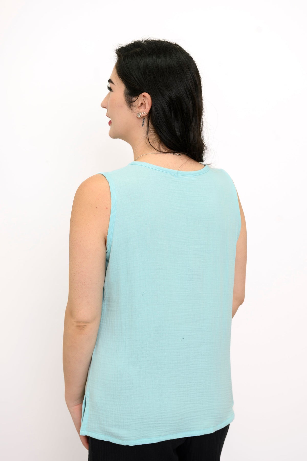 Woman wearing a light blue sleeveless top and black pants against a white background, back view