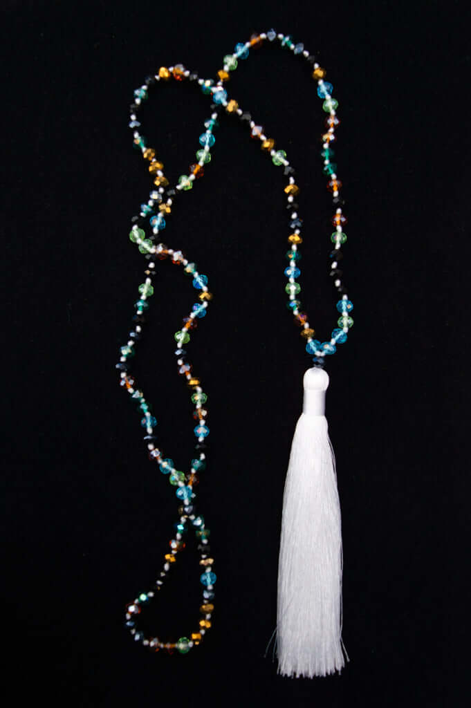 Handcrafted beaded necklace with multicolor gemstones and a white tassel on a black background