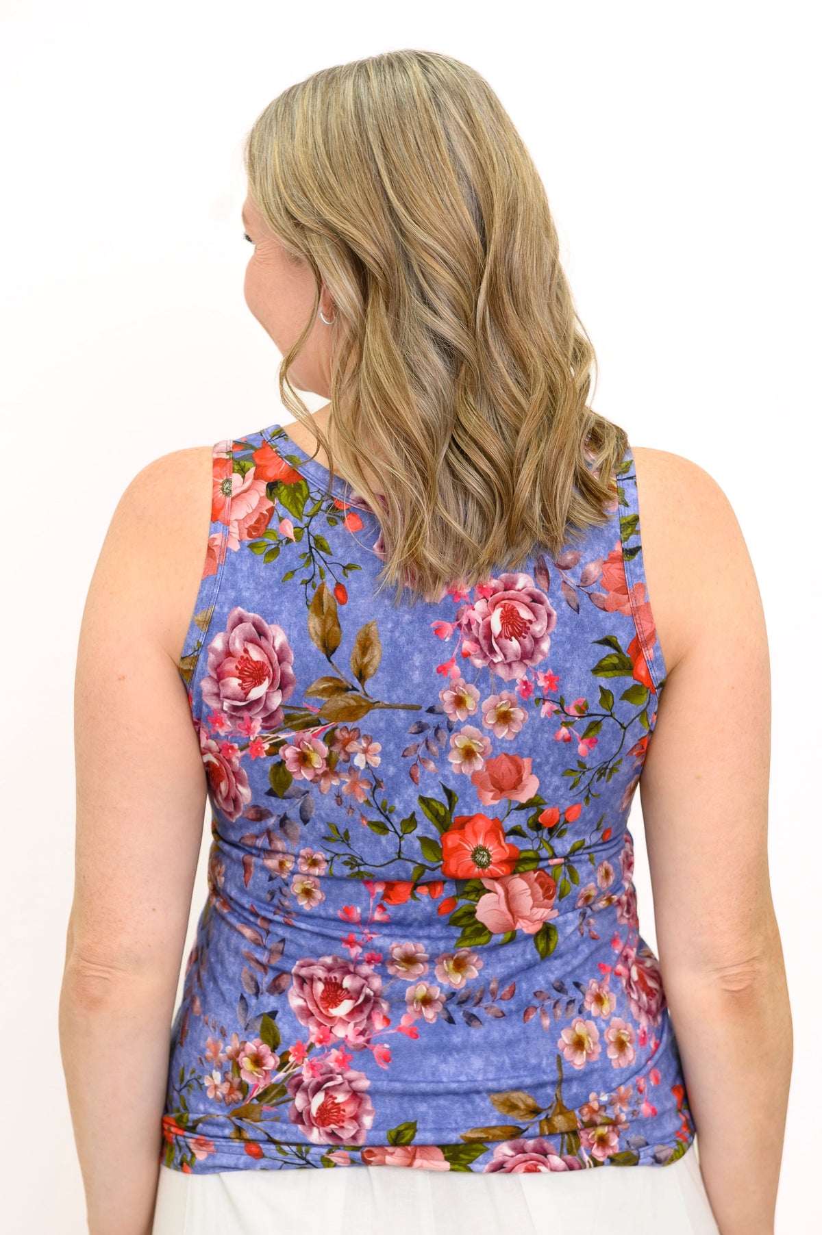 Back view of woman posing in sleeveless blue top with pink and red floral pattern