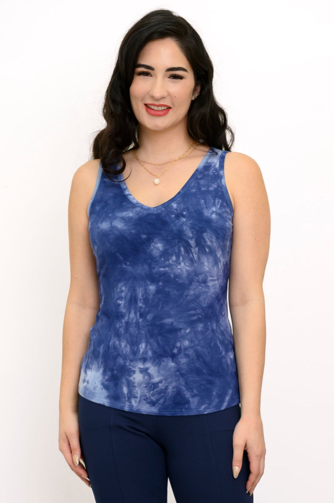 Woman wearing a blue tie-dye tank top and navy pants against a white background