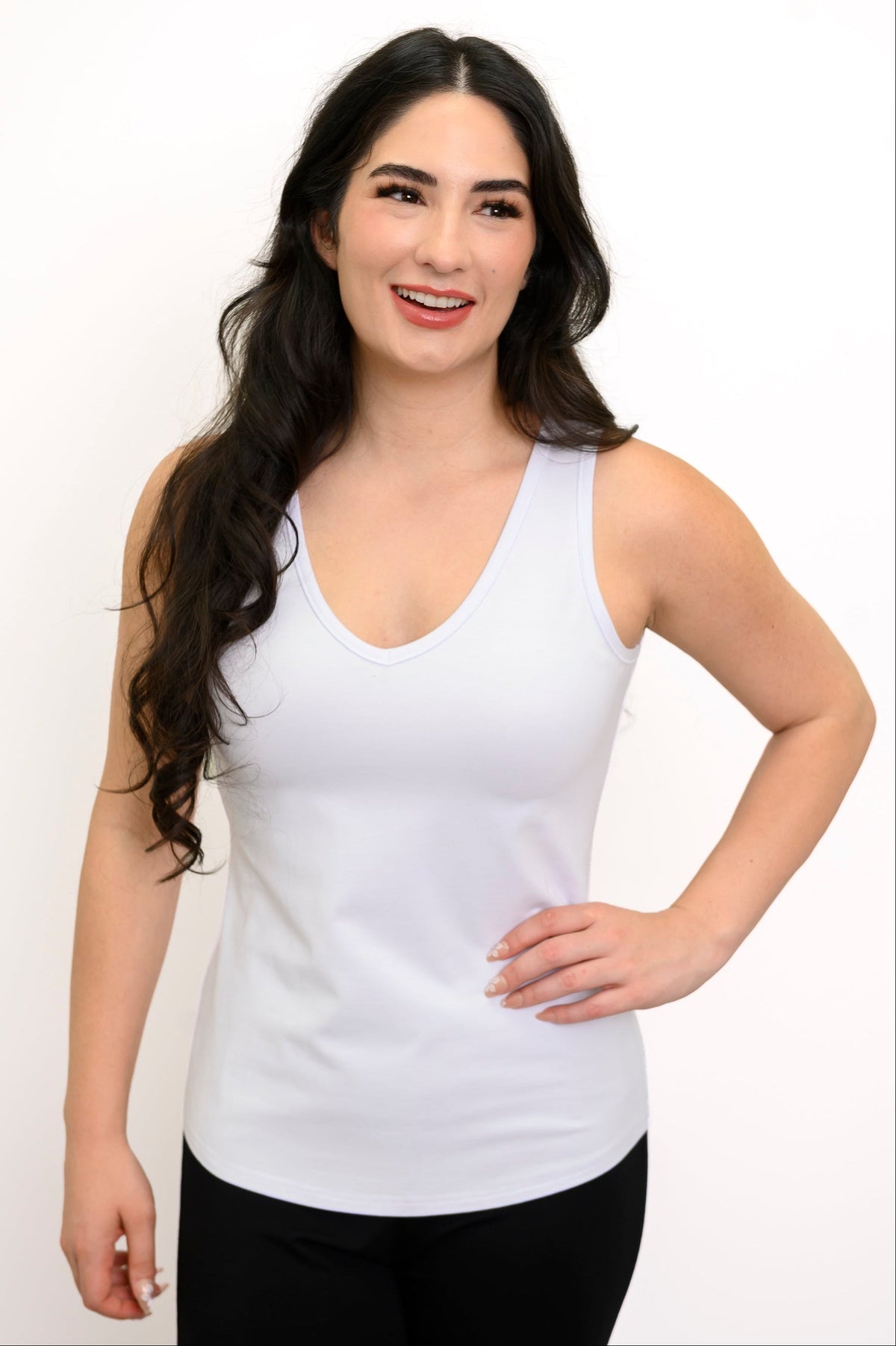 Woman smiling with her hand on her hip and modelling a white tank top with v-neck detail