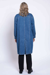 Back view of a woman wearing a knee length dark blue denim duster jacket in studio with black shoes.