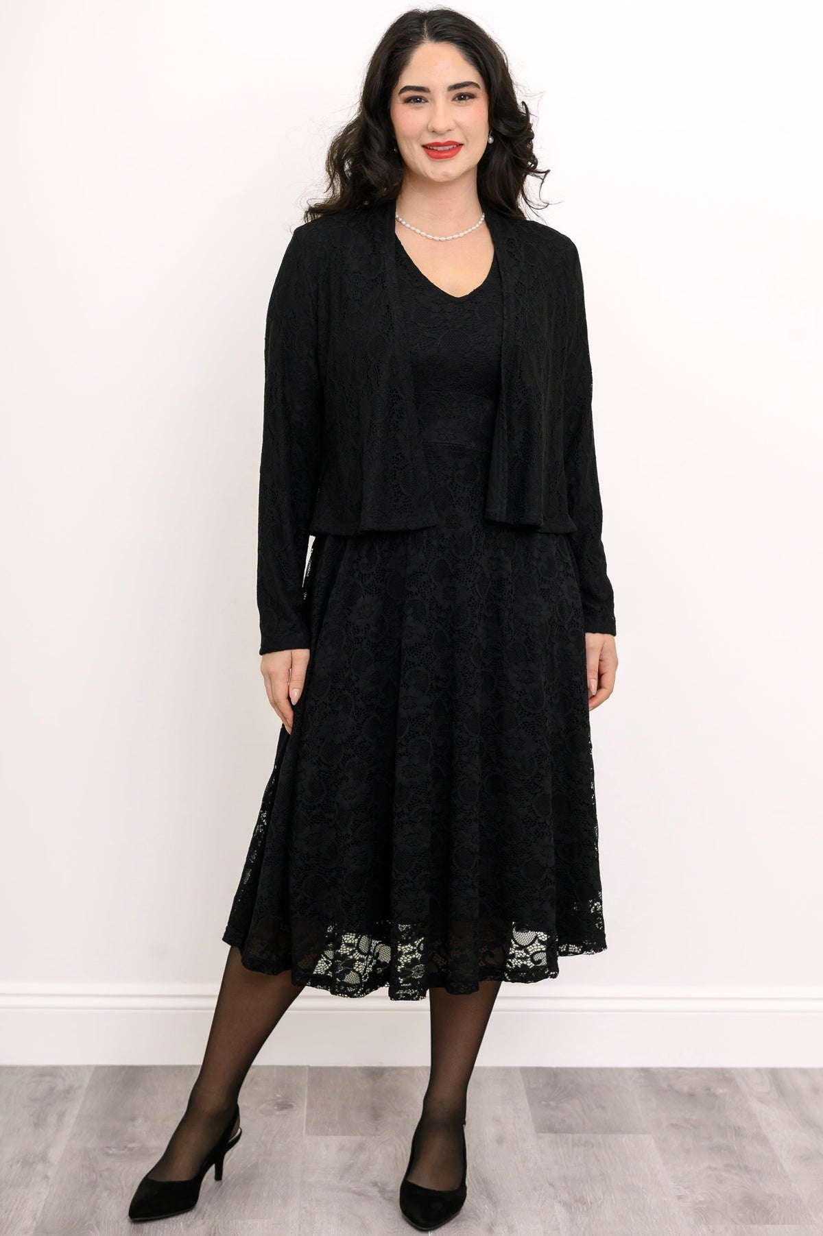 Front view of female model wearing a black lace dress with a matching jacket against a white background with gray floor