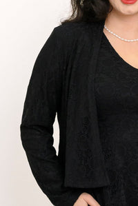A close-up of a female model wearing a black lace cardigan over a matching black lace top, accessorized with a pearl necklace against a plain white background.