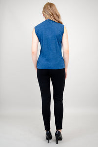 Back view of a woman wearing a sleeveless blue mock neck merino wool sweater with black trousers.