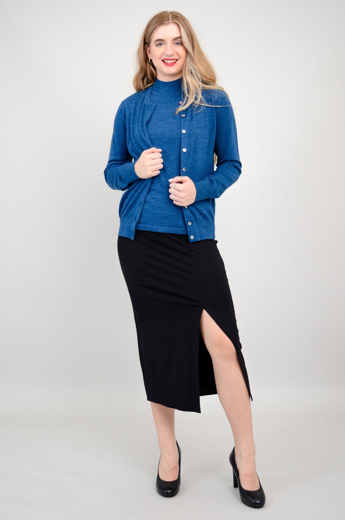 Woman modeling a blue button down sweater layered over a blue knit top and dark A-line skirt.