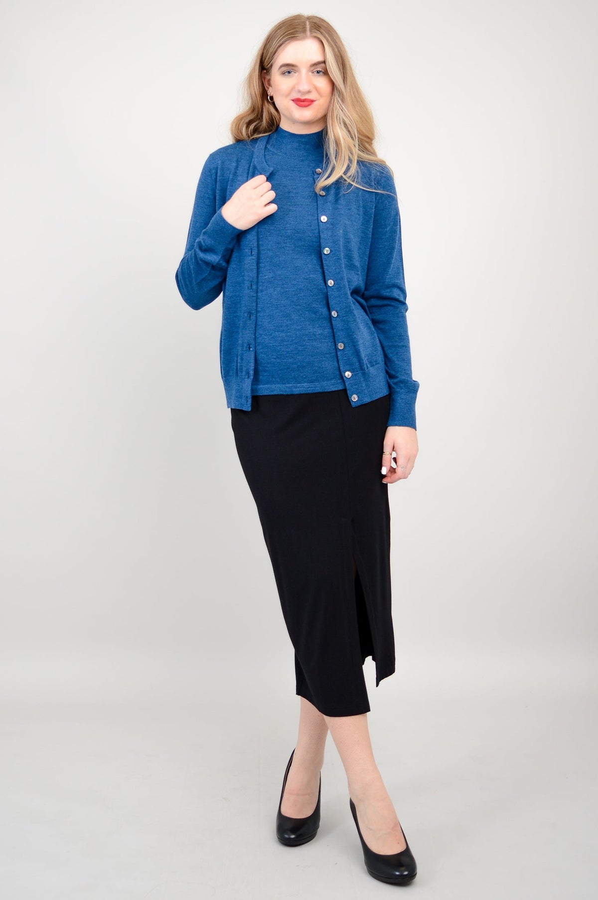Full length view of a woman wearing a blue merino cardigan over a matching blue top and black skirt.