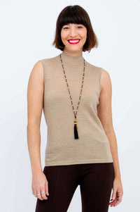Woman wearing a sleeveless tan mock neck sweater with dark pants