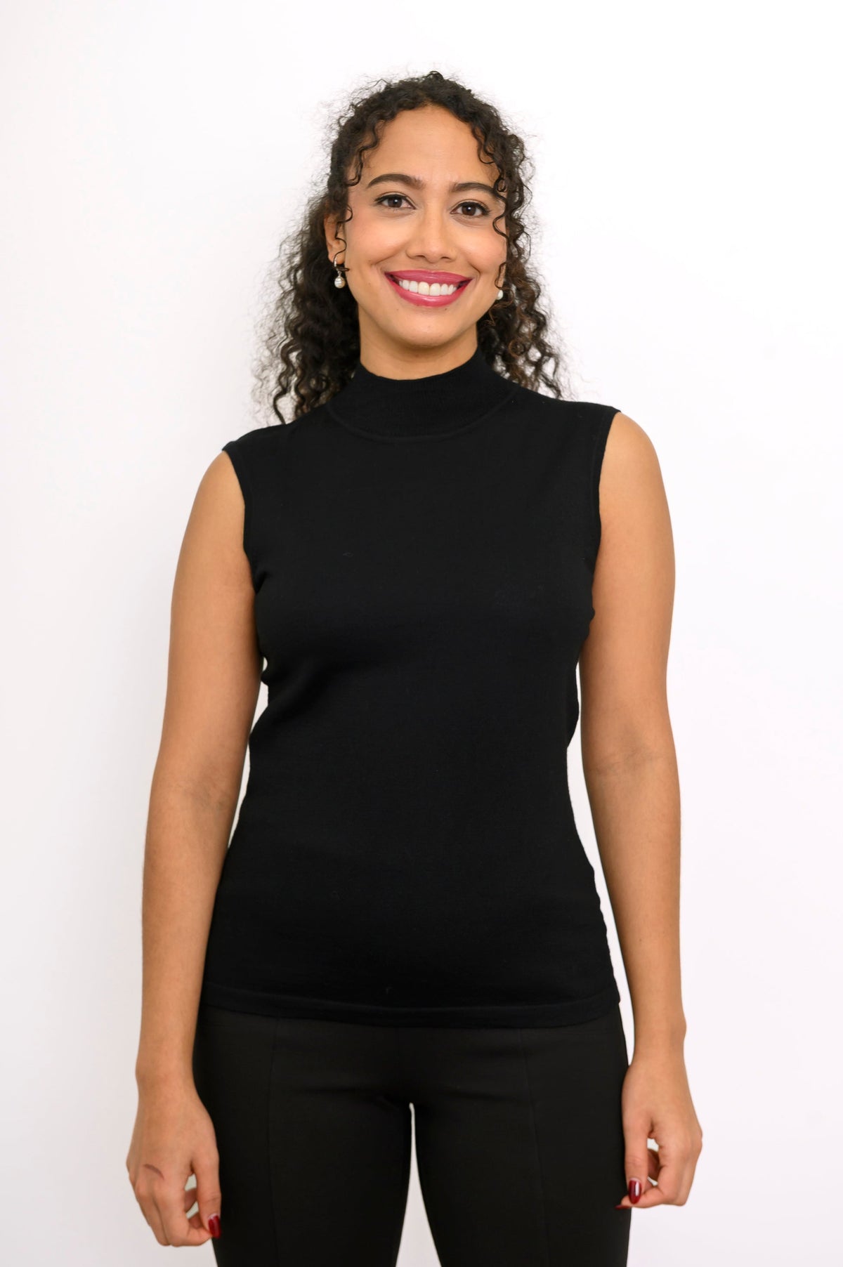 Close up front portrait of a smiling woman wearing a black sleeveless mock neck knit pullover top.