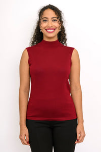 Close up front view of a woman wearing a burgundy merino wool sleeveless mock neck top and black trousers.