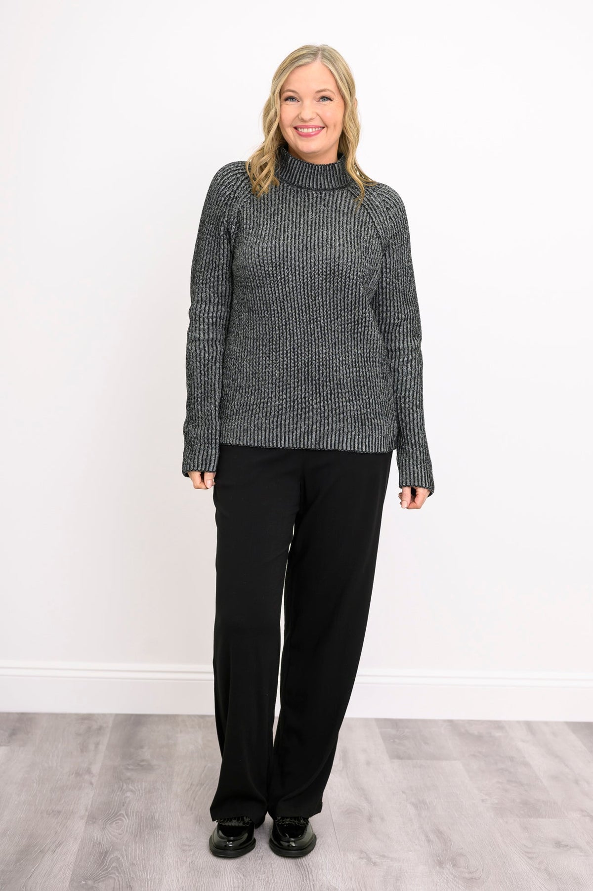Model posing with hand on hip in a loose charcoal gray cotton sweater, showcasing its soft, relaxed drape.