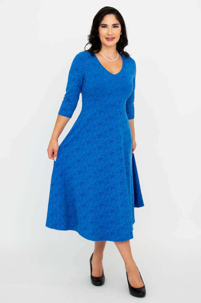 Woman showing A-line shape of royal blue midi dress with one hand holding the skirt
