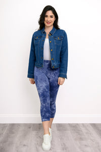 Front view of woman wearing a denim jacket over a white top and blue tie-dye print capri pants