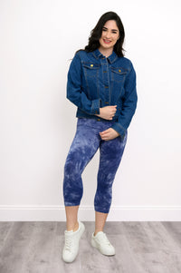 Full body view of woman posing in button-up denim jacket styled with blue tie-dye capri leggings