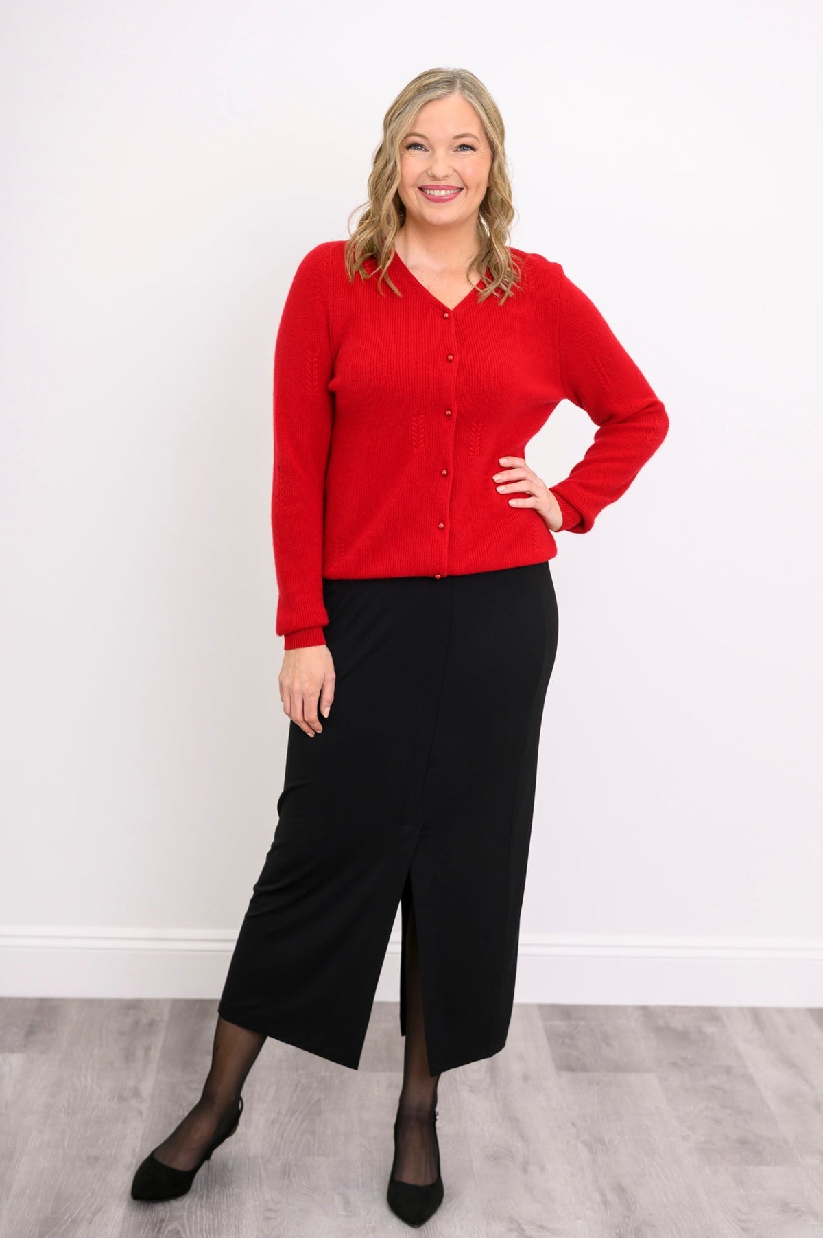 Woman modeling a bright red long sleeve button down cardigan sweater styled with a dark A-line skirt.