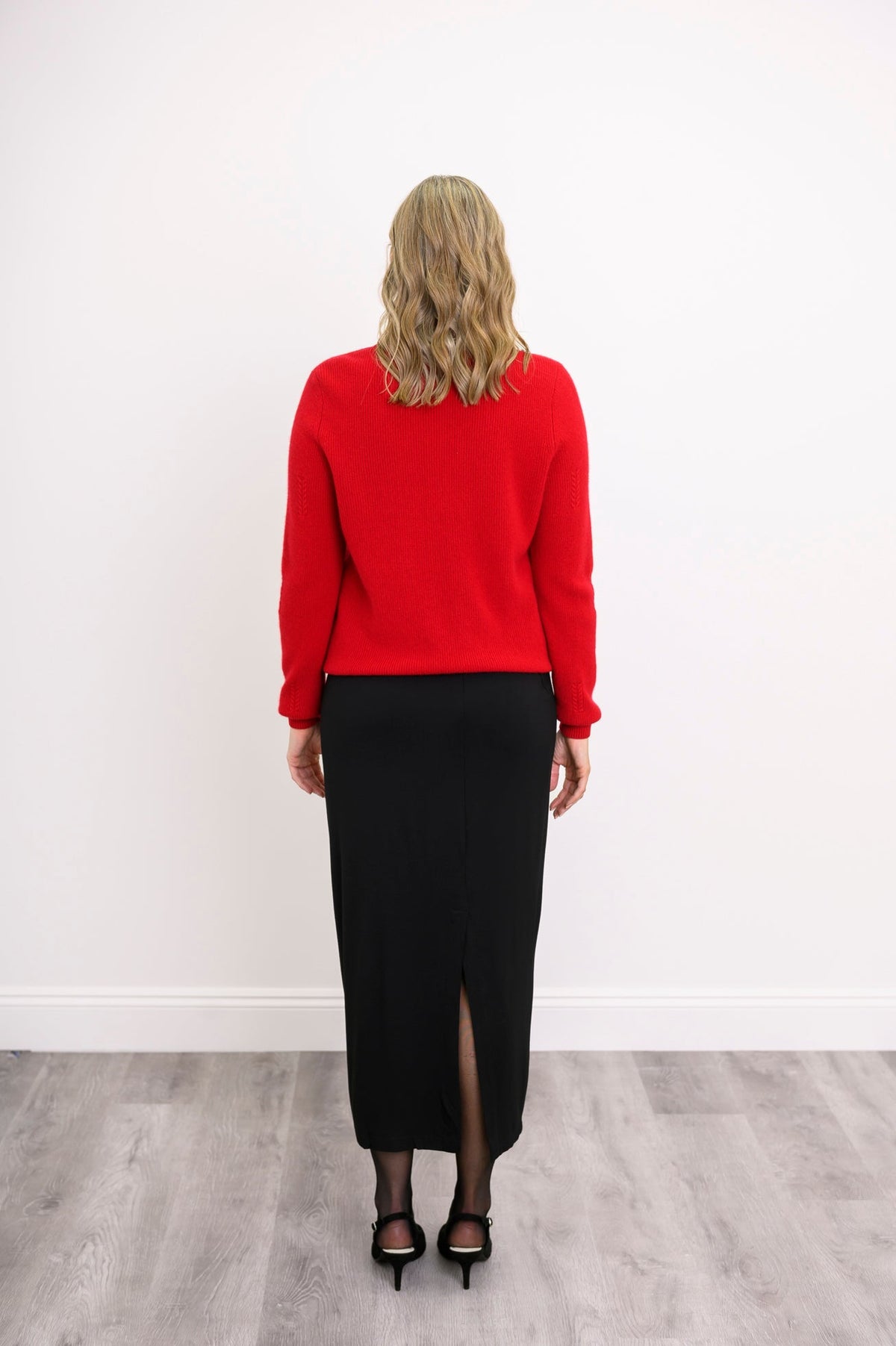 Three quarter angled shot of a woman modeling a red wool blend cardigan with red pearl button detail.