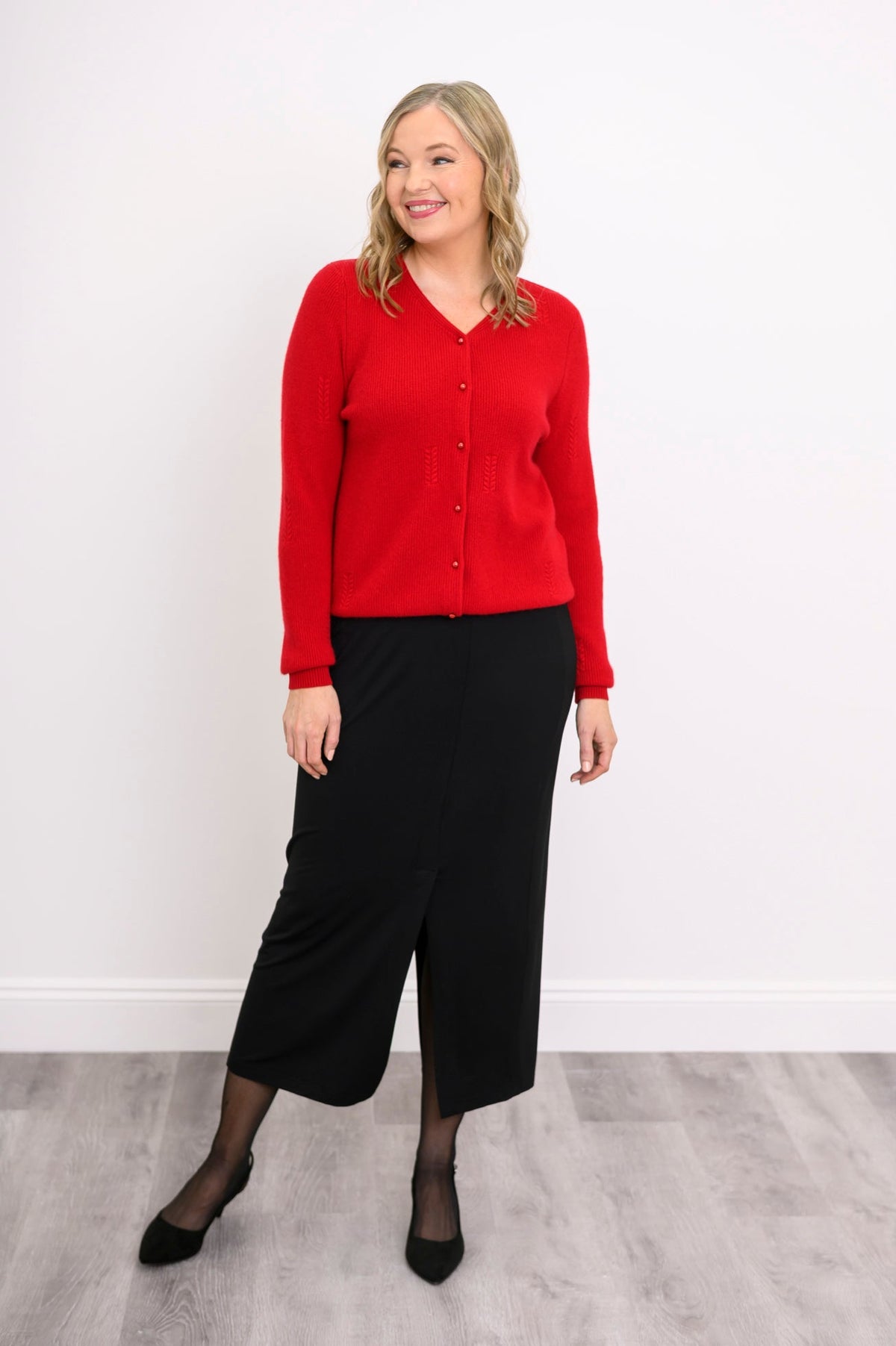front view of a model in a vibrant red ribbed hem v-neck cardigan sweater and black skirt.