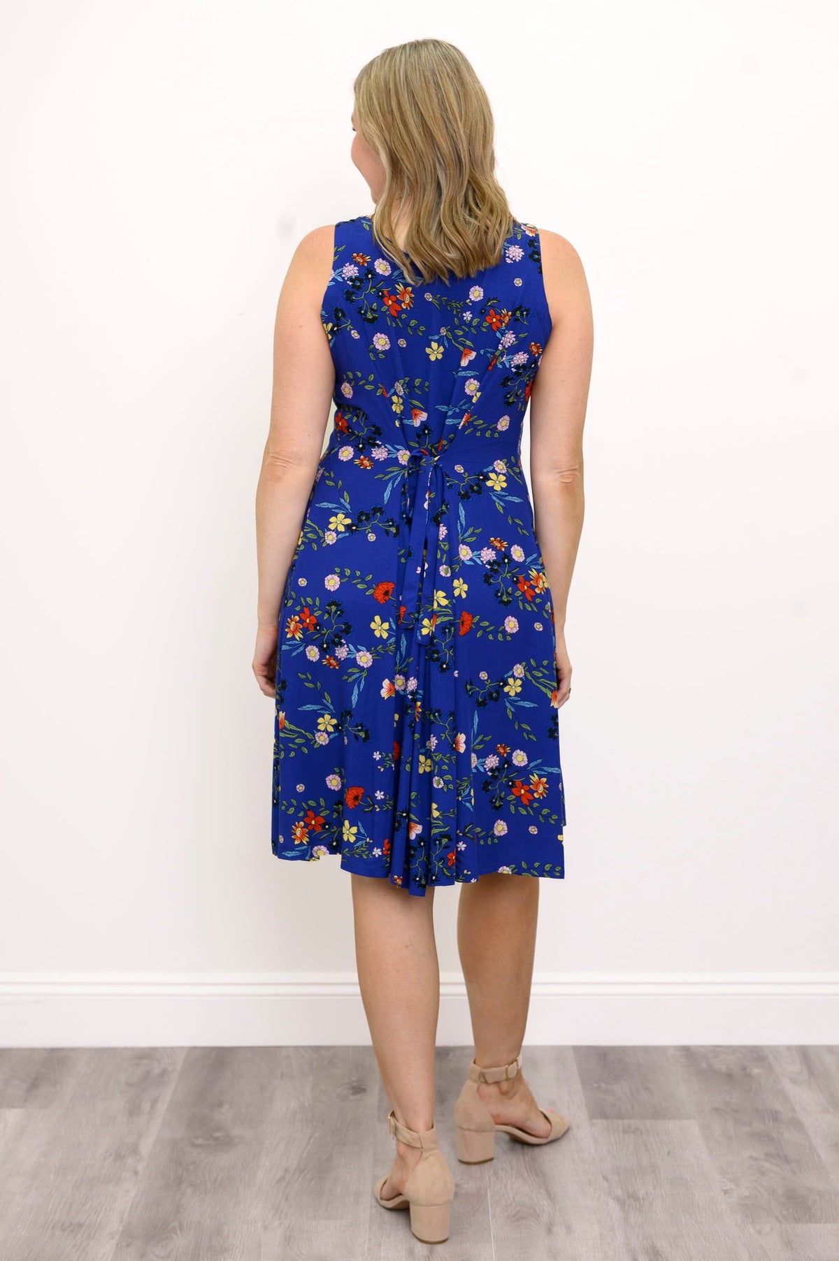 Back view of woman wearing a blue floral dress and sandals against a white wall 