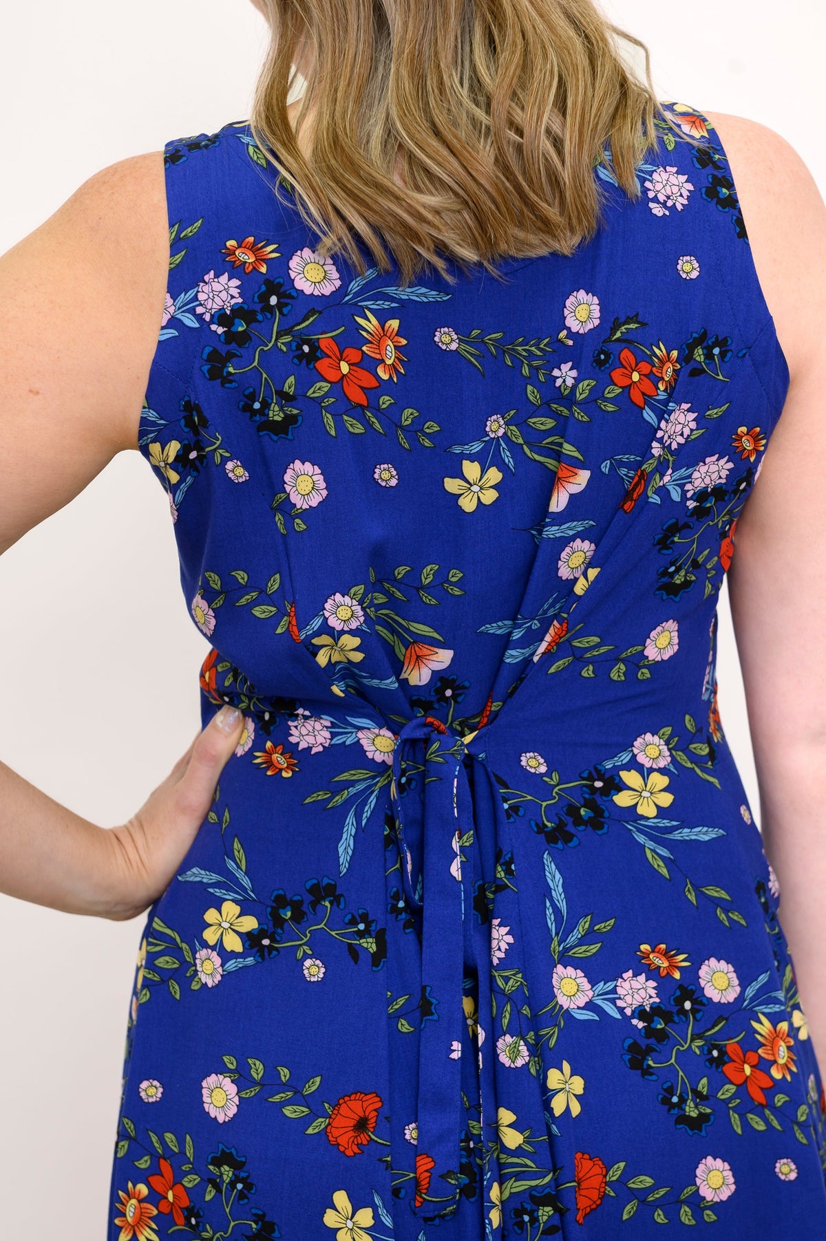 Back view of woman wearing a blue floral dress with ties at the back and a white background