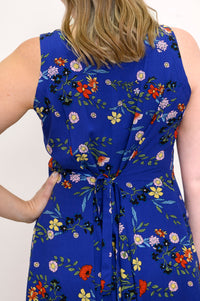Back view of woman wearing a blue floral dress with ties at the back and a white background