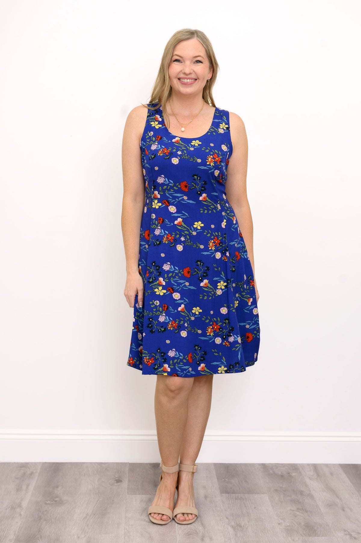 Front view of woman wearing a blue dress with red flowers and sandals against a white background