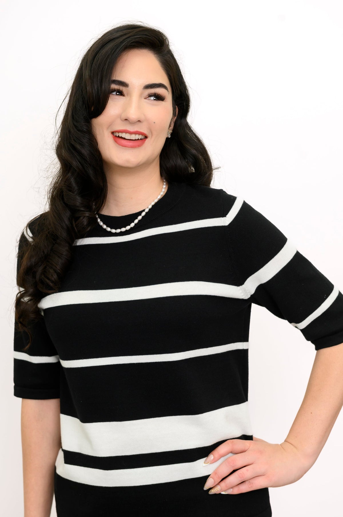 Close up front view of woman smiling and posing while wearing a black knit sweater with white stripes
