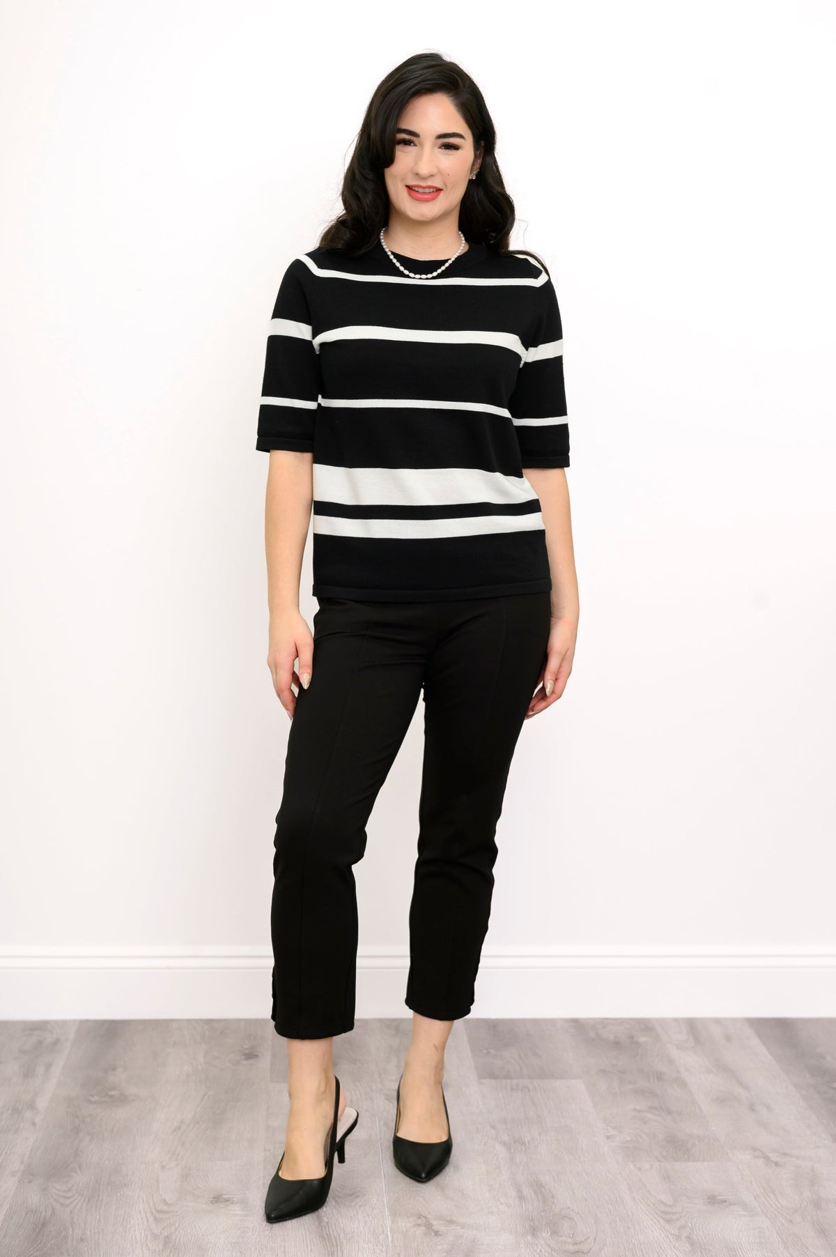 Full body front view of woman wearing a striped sweater and black pants against a white background