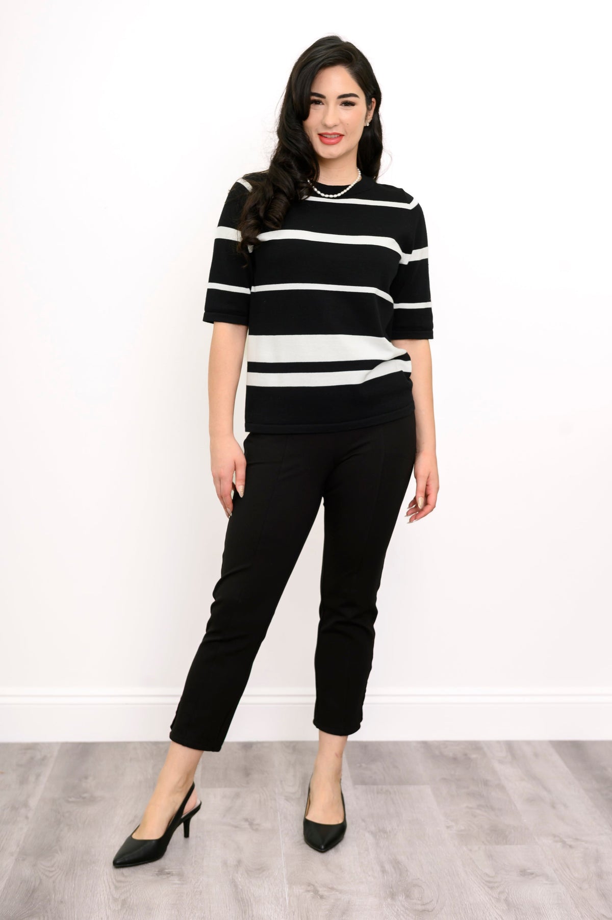 Full body view of woman posing in a black and white outfit and black heels