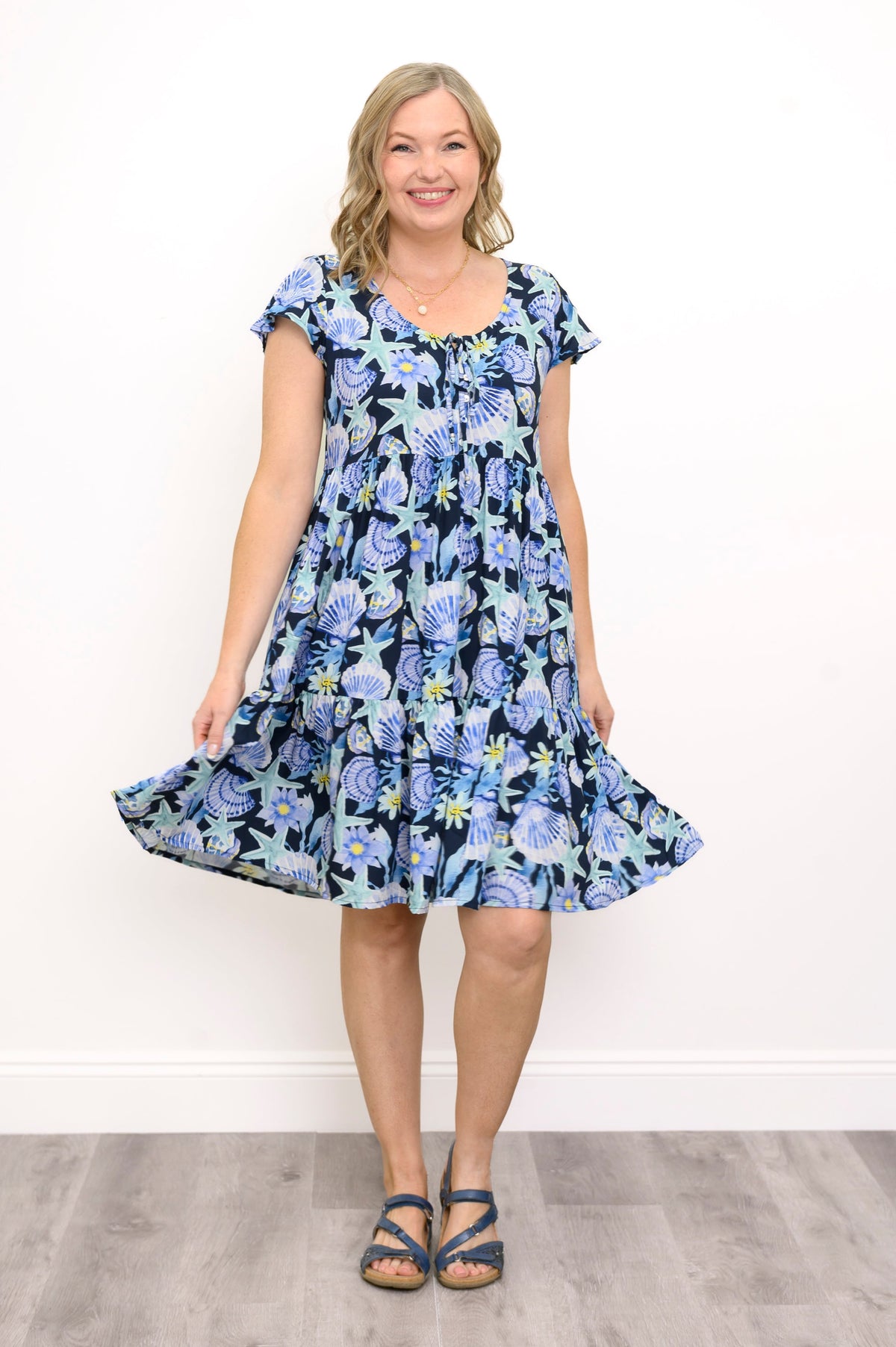 Front view of woman wearing a blue floral dress against a white background and sandals