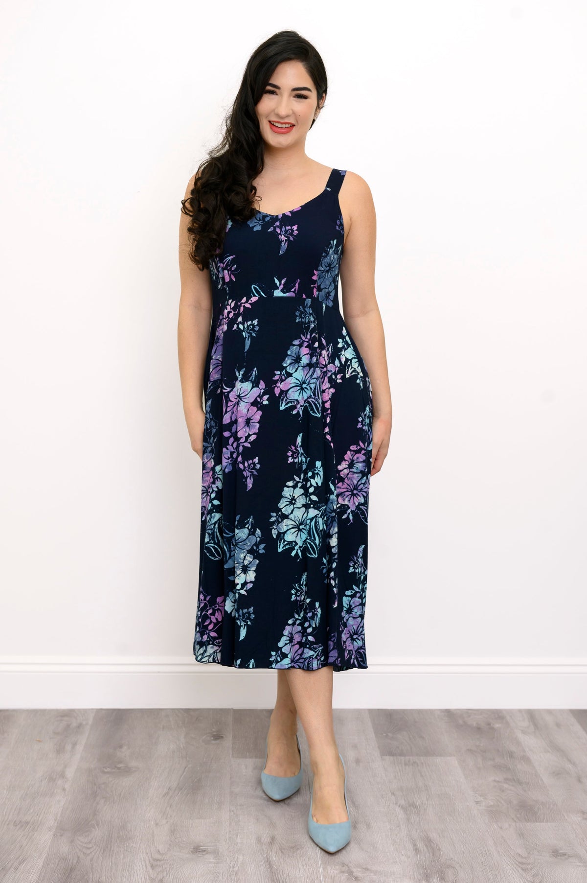 Woman wearing a blue sleeveless floral dress and blue shoes against a white background