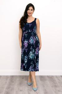 Woman wearing a blue sleeveless floral dress and blue shoes against a white background