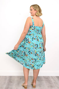 Woman wearing a blue floral dress with sandals and a white background, back view