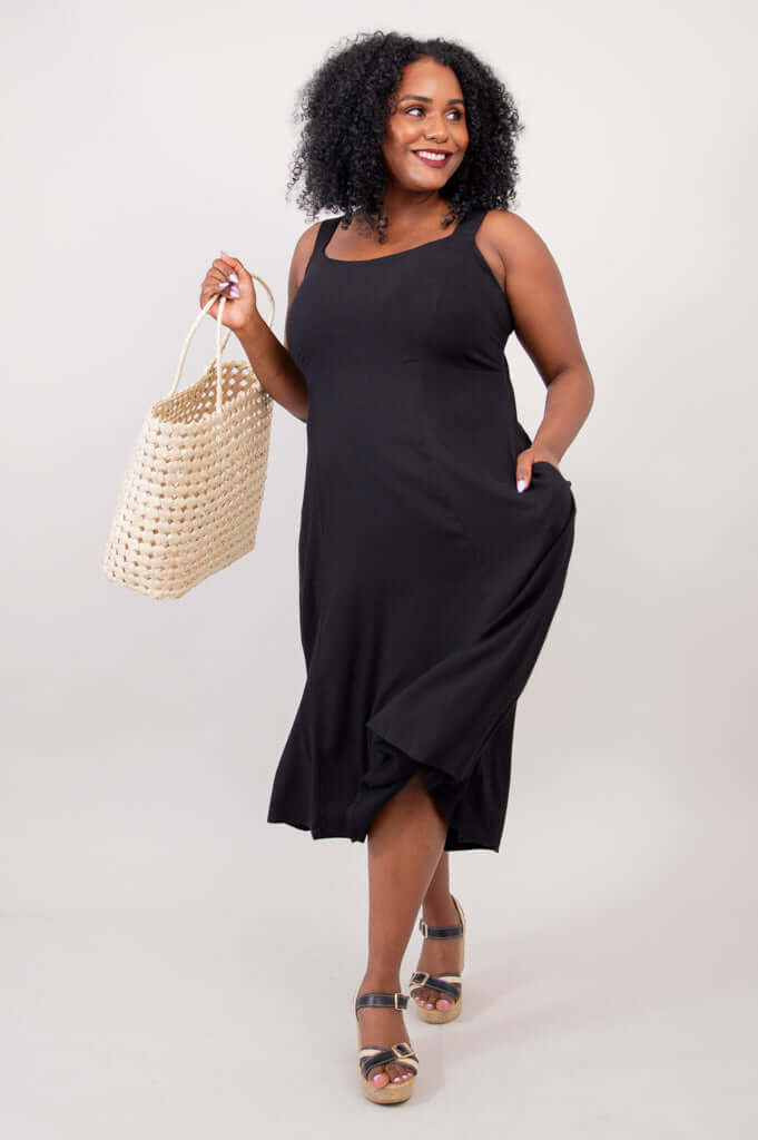 Model holding a woven bag while wearing the black A-line midi dress