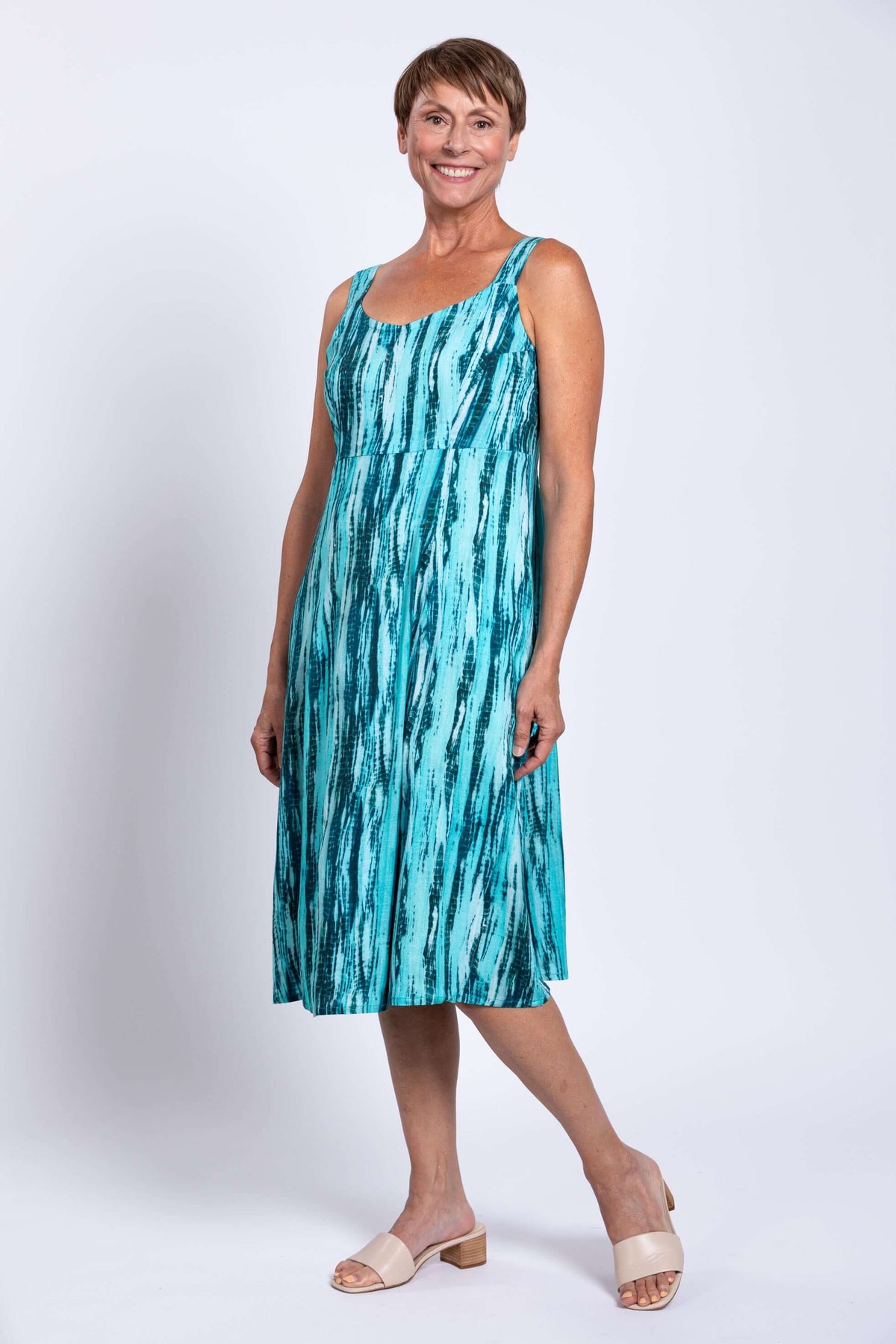Woman smiling and standing in teal streak sleeveless dress, front angle