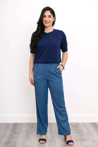 Full body view of woman in  indigo cardigan and blue pants, standing on wood floor