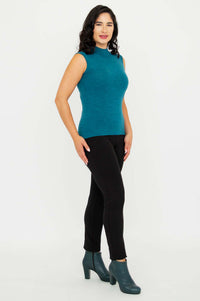 Side angle of woman wearing teal sleeveless mock neck sweater and black pants