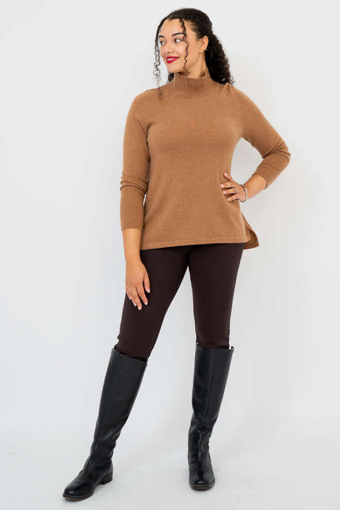 Angled full body view of a woman in a camel brown mock neck sweater looking to the side