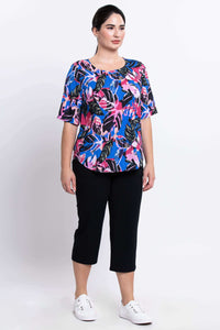 Full body angled view of woman modelling colorful botanical print top and black capri pants