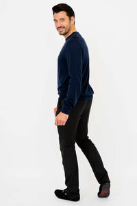 Man in navy blue sweater and black pants, turned sideways and smiling