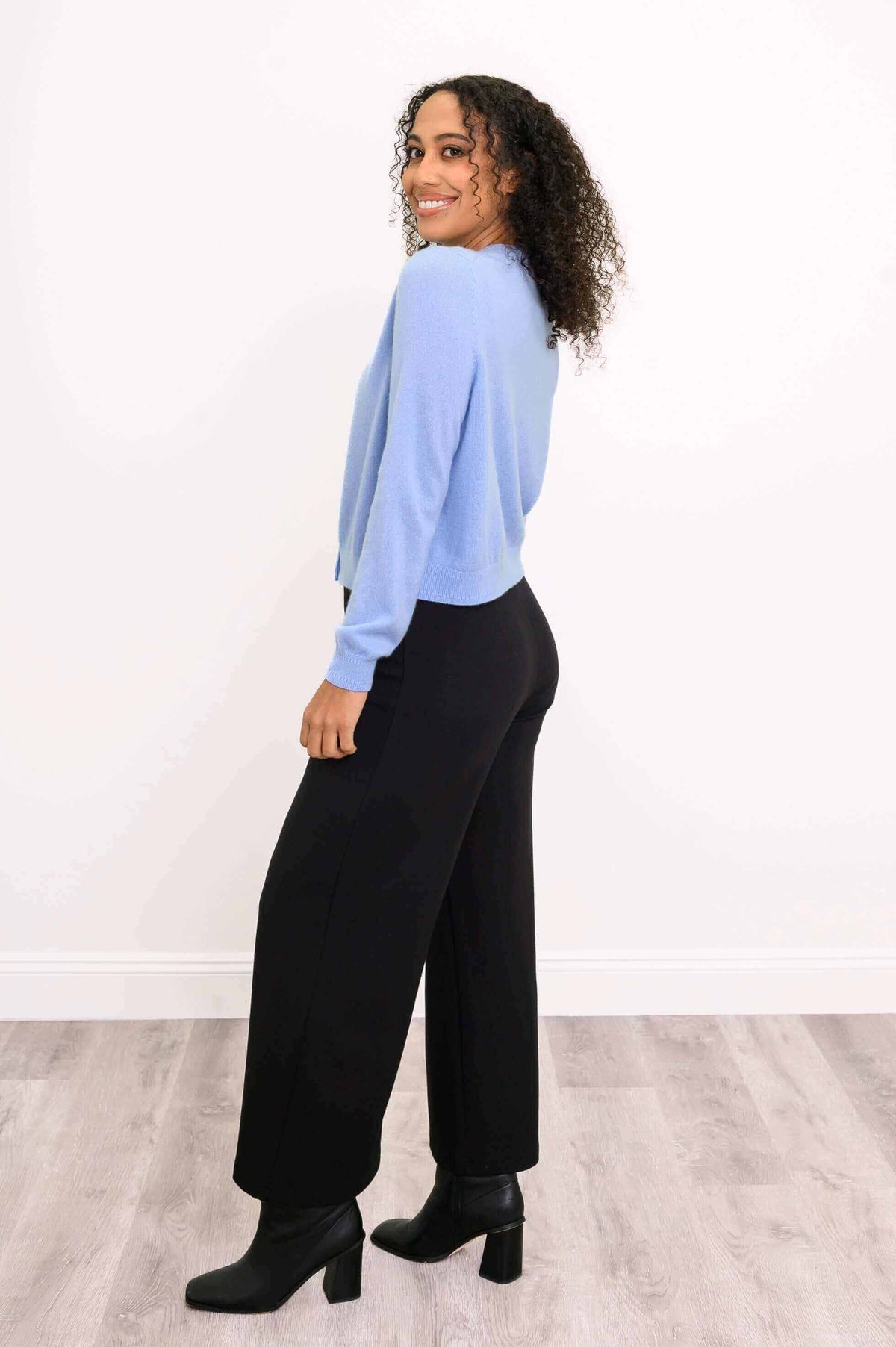 Side view of a woman showing the fit of a blue cashmere cardigan and black pants