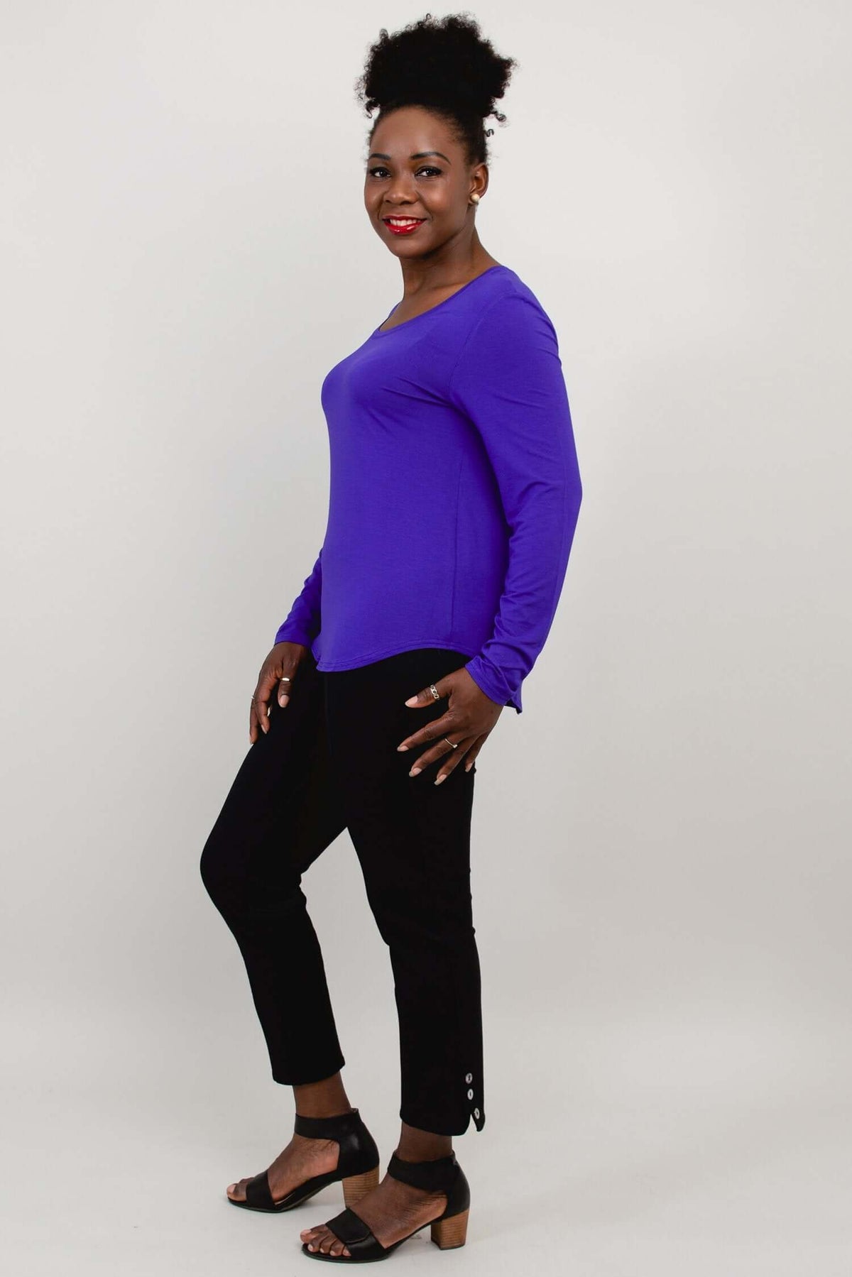 Side view of woman wearing a purple long sleeve shirt and black pants