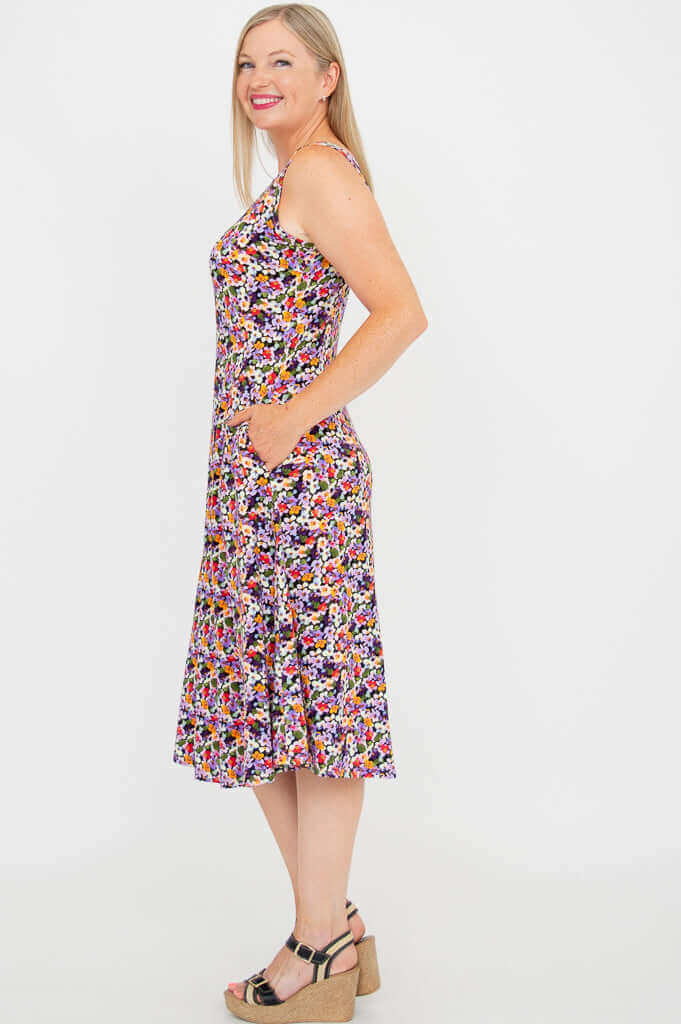 Side view of model in vibrant floral sleeveless dress with pockets