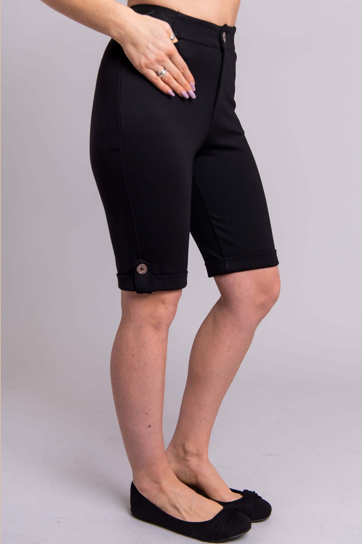Side view of model wearing black Norma tailored shorts showing buttoned cuff