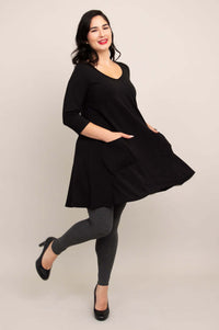 Side view of model twirling in black A-line tunic dress and grey leggings