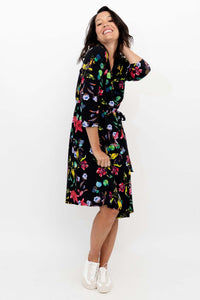 Side view of a woman in a black floral wrap dress smiling and posing