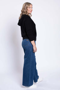 Side view of model wearing wide-leg blue denim jeans with black zip-up hoodie and white sneakers