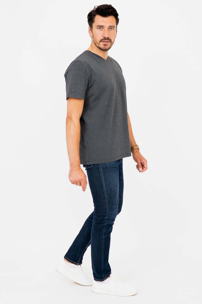 Side walking view of man in dark grey V-neck T-shirt with jeans and white shoes