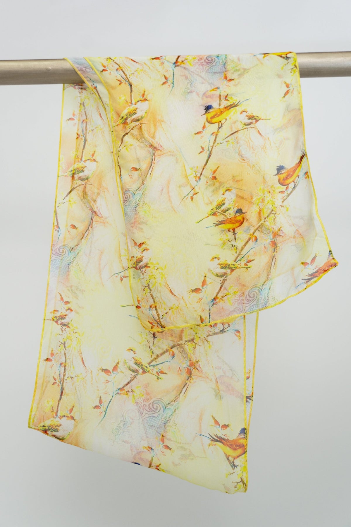 A large silk scarf with a bird pattern in yellow, green, and other colors, displayed on a white background, front view
