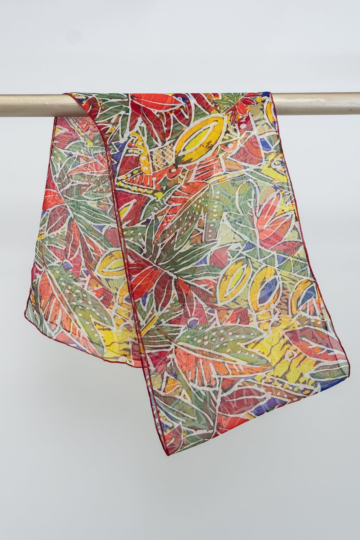 A vibrant multicolored silk scarf with an abstract tropical pattern displayed on a rack, front view